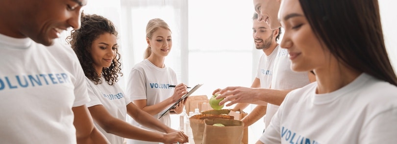 Volunteers assisting one another with food, listing items on a paper bag