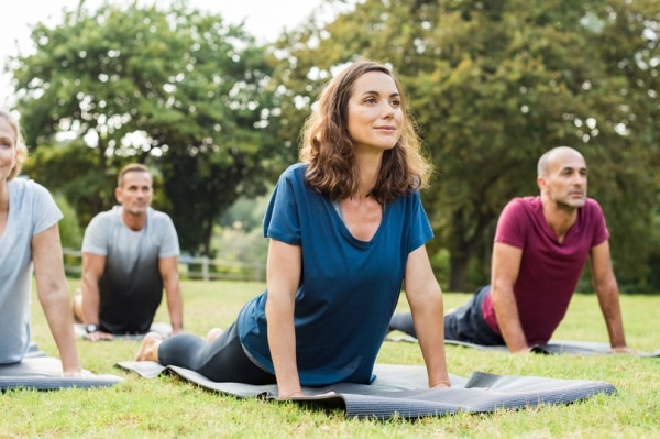 A diverse group of people practicing yoga in a park, surrounded by trees and enjoying the fresh air