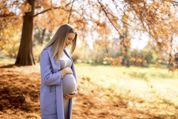 Pregnant woman standing outside in the classic pose of holding her hands on the top and bottom of her abdomen