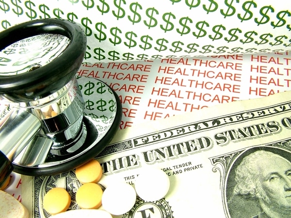 Image with a dollar bill and dollar signs alongside a stethoscope and pills, with the text healthcare in the background