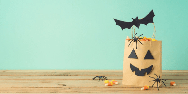 Halloween themed gift bag holding candy corn, with small fake spiders and paper bat attached