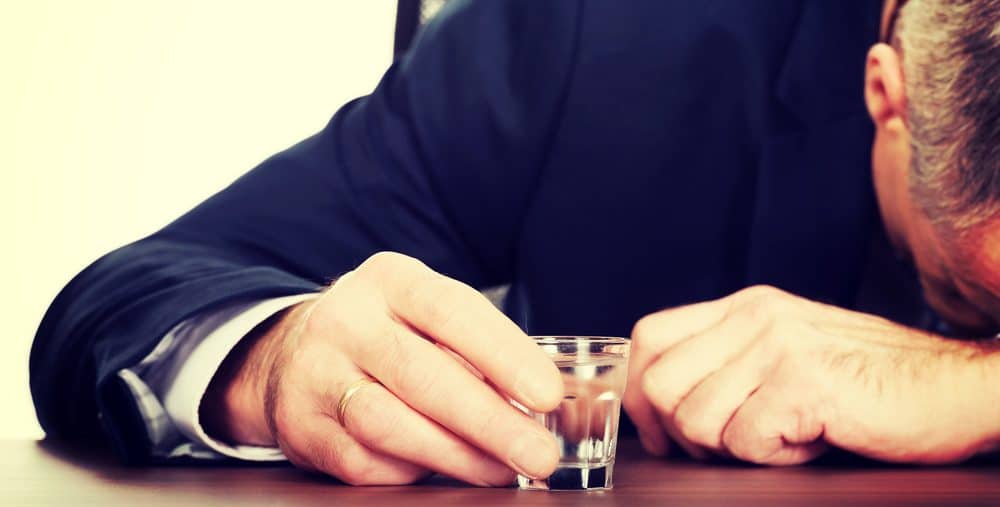 Man face down on table resting his head on his arm while holding a shot glass
