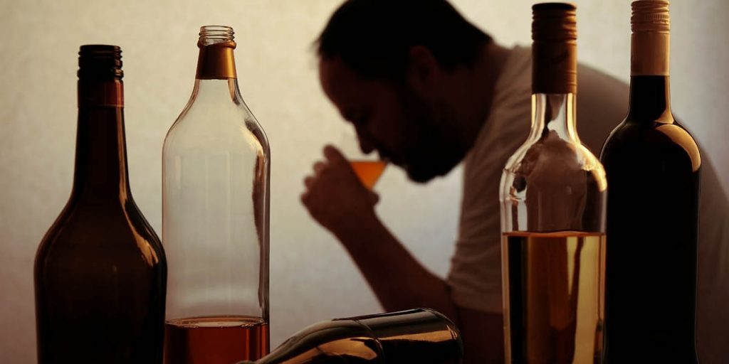 A drinking man shown in silhouette behind a number of liquor bottles