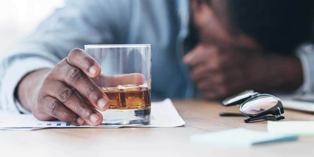 Man holding glass of booze laying his head on a table