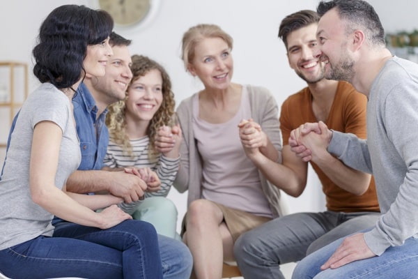 Group therapy session showing everyone holding hands and smiling together