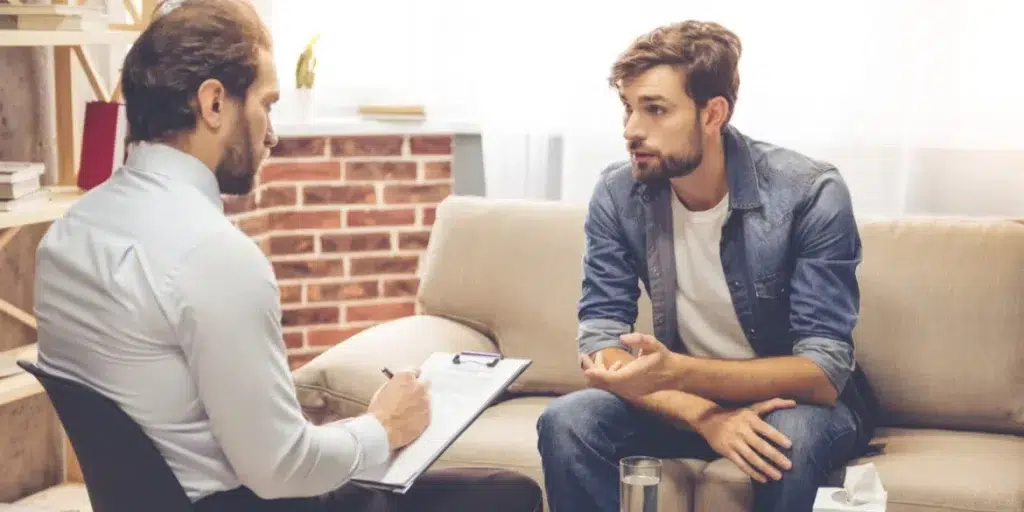 Interviewer taking notes while talking to man, both holding pen and paper