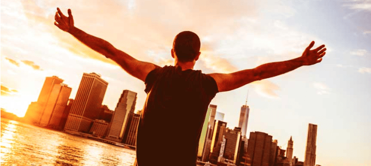 A man joyfully stretches his arms in front of a city skyline, embracing the urban beauty surrounding him