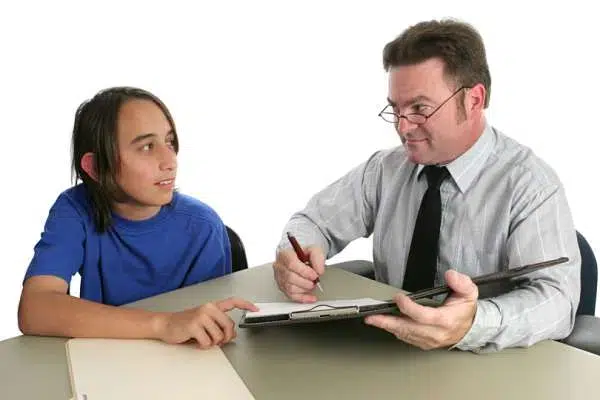 A teacher and a student sitting at a table with a clipboard, engaged in a discussion