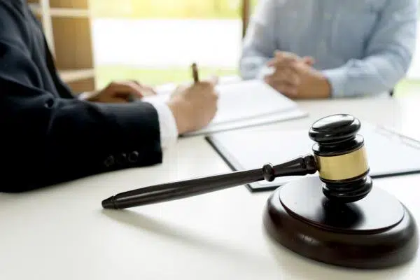 A lawyer and client in a meeting, with the lawyer signing on the paper and a court gavel beside them