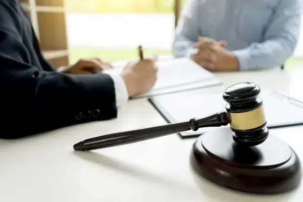 A lawyer and client in a meeting, with the lawyer signing on the paper and a court gavel beside them