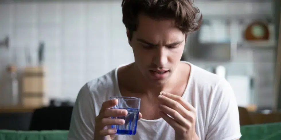 A man holding a glass of water, taking his medicine