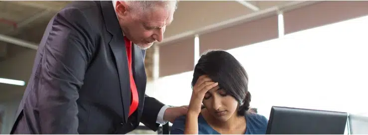 A concerned man in a suit looks at a woman on a laptop, offering comfort while holding his head
