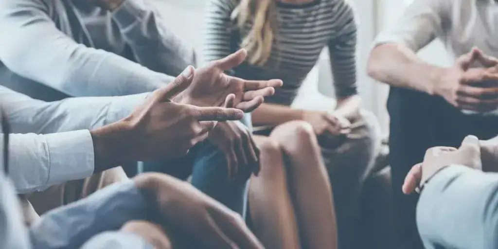 A diverse group of individuals engaged in a conversation, sitting in a circle and using hand gestures to communicate effectively