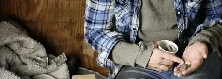 A homeless man sits on the floor, holding a cup, counting money