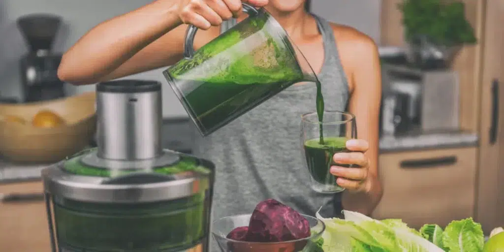 Woman pours green juice into a drinking glass, preparing a healthy shake