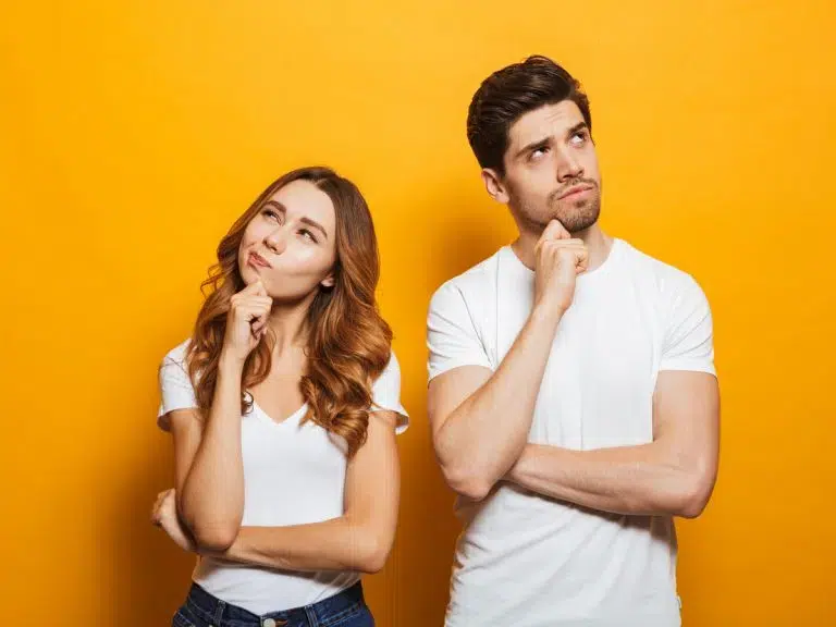 A man and woman standing against a yellow background, deep in thought