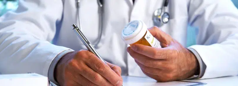 A doctor writing notes while holding a medicine bottle