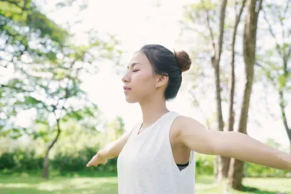 An Asian woman meditating in the park, stretching her arms out