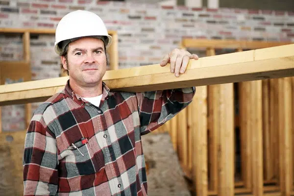 A man in a hard hat holding a wooden beam at a construction site