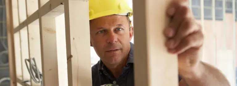 A worker in a hard hat inspecting wood alignment