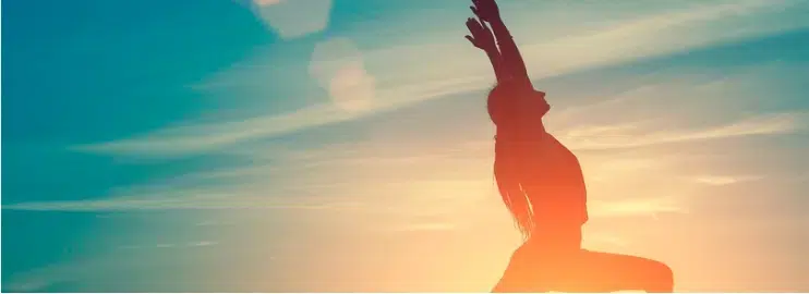 A woman gracefully performs a handstand on a beach at sunset, showcasing her flexibility and strength