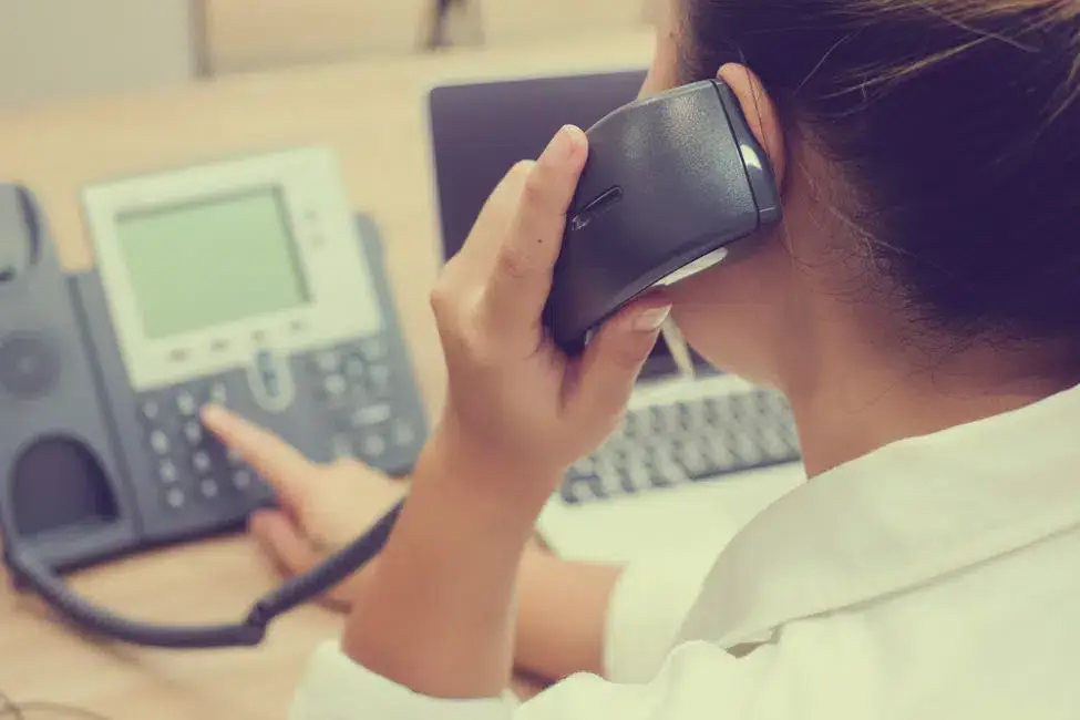 A woman sitting at a desk, talking on the phone while dialing