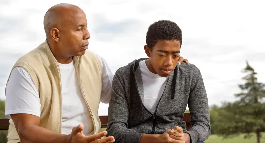 A father and his son sitting on a bench, with the father engaged in conversation and guiding his son