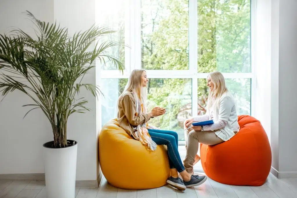 Two girls sitting on bean bags, engaged in conversation, near a window