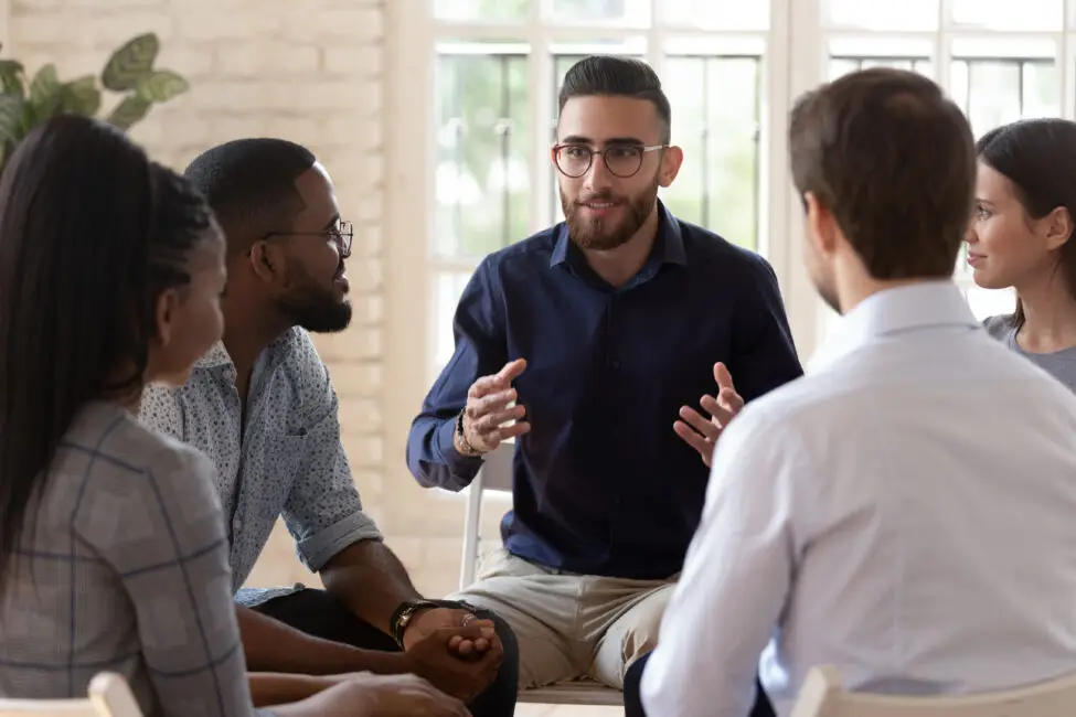 Group of individuals engaged in a discussion, with a man using hand gestures to communicate